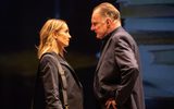 Portrait photo of Joanne Froggatt and Robert GlenisterJoanne Froggatt and Robert Glenister. They're both in smart blazers and Joanna has a leather bag on her shoulder. They're close and facing each other. Robert has his hands on his hips. On the screen behind you can just see a projection of a stack of books.