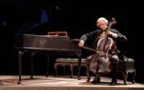 Samuel Blenkin is sat next to a Harpsicord playing a cello.