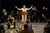 BoD 2-050 Centre stage, Ayesha Dharker (brown hair tied back, beige suit dress), stands at a wooden podium arms outstretched as she speaks to a room of teachers and students.