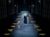 BoD 2-229 Two rows of wooden boxes line each side of the stage. Holly Atkins (dressed as a nun),holds Samuel Creasey (patterned jumper and plain khaki coat) by the ear. Left is Heather Forster crouching behind a box with a paper puppet of a cat facing the other two.