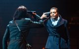 Production photo of Julius Caesar. Taken from behind Michelle Fairley we see her and Adjoa Andoh, both in black coats, both with their right hand holding a gun to their own heads.