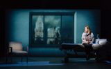 Production photograph from My Name is Lucy Barton. Laura Linney is sat on a hospital bed looking to the side at an empty hospital chair. Behind the scene is large hospital window frames with a projection of the city through it, you can see the Empire State Building.