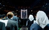 Gwendoline Christie wears a severe black robe and stands in a glass box, watched by the other cast members