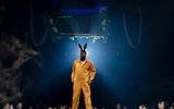 Hammed Animashaun, wearing a yellow jumpsuit and donkey ears, stands backlight by a spotlight