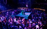 Gwendoline Christie and Oliver Chris dance on a platform stage, surrounded by audience members