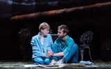 Garden at night. We see the large copper pipe across in the background. Claire Skinner is kneeling and Sion Daniel Young sat next to her. They have their hands clasped in each others and are looking at eachother worried. There's papers spread out across the grass in front of them.