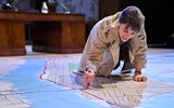 Siobhán Cullen kneels on the floor, she is drawing in red pen on a huge map of New York which covers the floor. She's wearing a trench coat and is clenching her teeth.