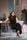Two Ladies Zrinka Cvitešić is sat in a metal chair next to a long table. She's wearing a long smart black dress with snakeprint heels. Her legs are crossed and she is holding her hands and arms out as if asking a question with great emphasis.