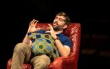 James Corrigan leans back in a red leather armchair, holding a green cushion on his lap