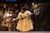 l-r Johnetta Eula'Mae Ackles (Marjory) photo Manuel Harlan (2) Shot of Johnetta Eula'Mae Ackles who's wearing off white blouse and skirts. Sh'es leaning over slightly with her right arm out as if curtseying and in her left hand is a huge magnifying glass. Behind her is the attic set with a wooden ladder leant against the back of the set and puppets hanging up.