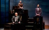 Lyndsey Marshal, Eben Figuieredo and Simon Russell Beale sit on top of a wooden trunks with their hands in their laps.