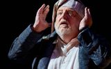 Simon Russell Beale looks upwards with his hands on either side of his face, he wars a nightcap and gown.