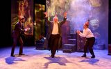 Eben Figueiredo, Simon Russell Beale and Lyndsey Marshal are dancing together. Simon is in the middle with his hands in the air and the other two are either side of him clapping. They're all wearing cardboard Christmas hats