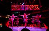 The Hot Box girls dance, their arms outstretched, in the Hot Box club