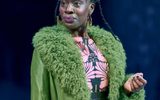 Ony Uhiara stands wearing a green coat with a patterned pink dress.