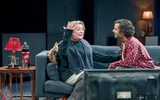 Clare Higgins and Sebastian De Souza laugh together on a sofa, Clare looks bemused as Sebastian watches her fondly.