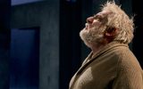 Simon Russell Beale stands looking upwards deep in though, his hair is messy and he wears an old beige cardigan.