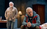 Simon Russell Beale stands with his hands in his pockets, he wears an old beige cardigan. Michael Simkins sits with his hands clasped in front of him, he does not face Simon.