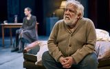 Simon Russell Beale sits slouched, wearing a beige cardigan, his hands clasped in his lap