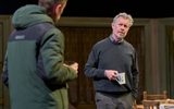 Alex Jennings stands with ceramic mug in his hand smiling. He wears a grey jumper and trousers.