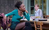 Racheal Ofori sits at a table, she wears a long sleeved top with a sparkling green skirt.