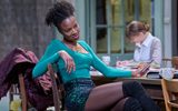 Racheal Ofori sits at a table, she wears a long sleeved top with a sparkling green skirt.