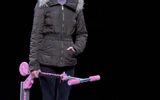 Sarah Twomey stands holding a pink children's scooter, she has a blank expression on her face and wears a puffer jacket.