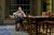 Sthbry-169 Phoebe Nicholls sits at wooden table with her hands clasped and looks sad.