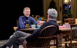 Josh Finan and Alex Jennings sit at a wooden table cluttered with board games and mugs. Josh laughs, leaning across the table and Alex leans back in his chair with a glass. They are playing Kerplunk.